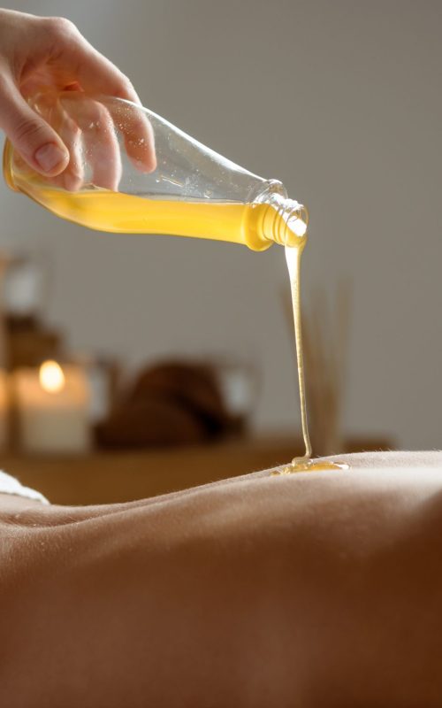 Honey pouring on girl's naked back in spa salon. Copy space.